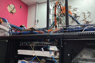 An image from the report of a college’s server room with wires everywhere and paint damage from Hurricane Maria.